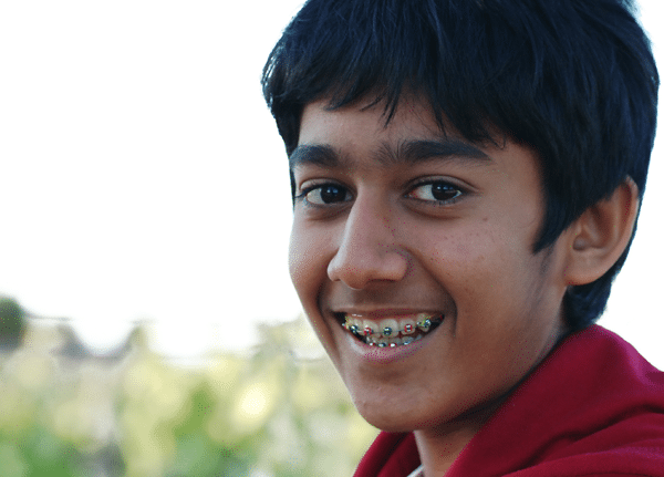 Teen girl smiling with metal braces. Compare Invisalign vs braces for straighter teeth.