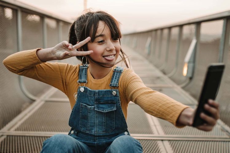 Young girl taking selfies on a bridge with a great smile because growing children with braces Invisalign or clear braces to fix their smile sets them up for a lifetime of healthy smiles.
