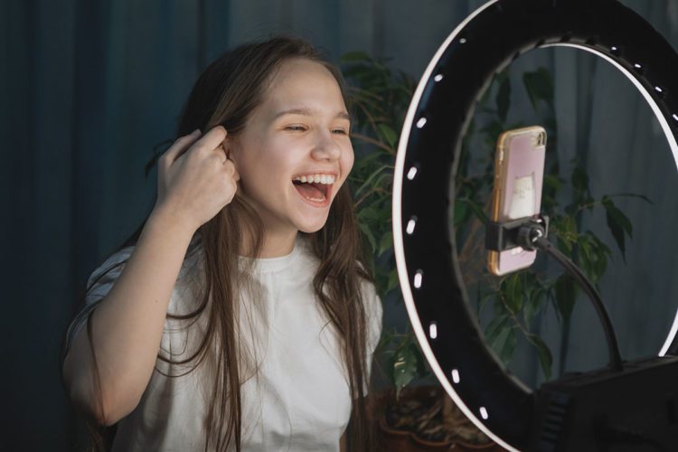 A young girl brushing back her hair and smiling after Invisalign First orthodontic treatment while making a video for social media.