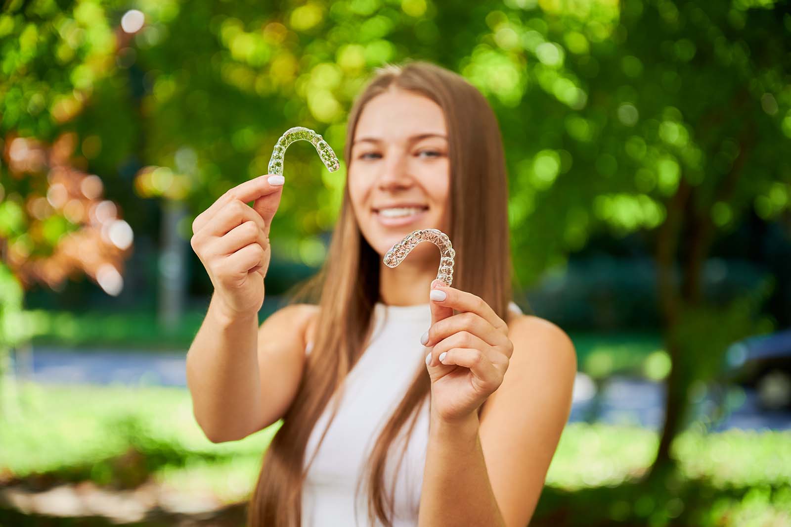Learn the facts about Invisalign vs Smile Direct Club smiling woman holds up two clear aligners