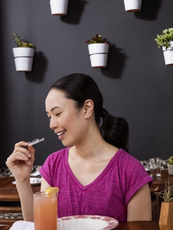 Woman holding aligner in cafe Invisalign