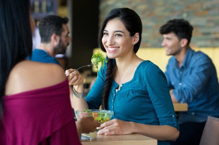 Woman eating salad in a restaurant with her friend