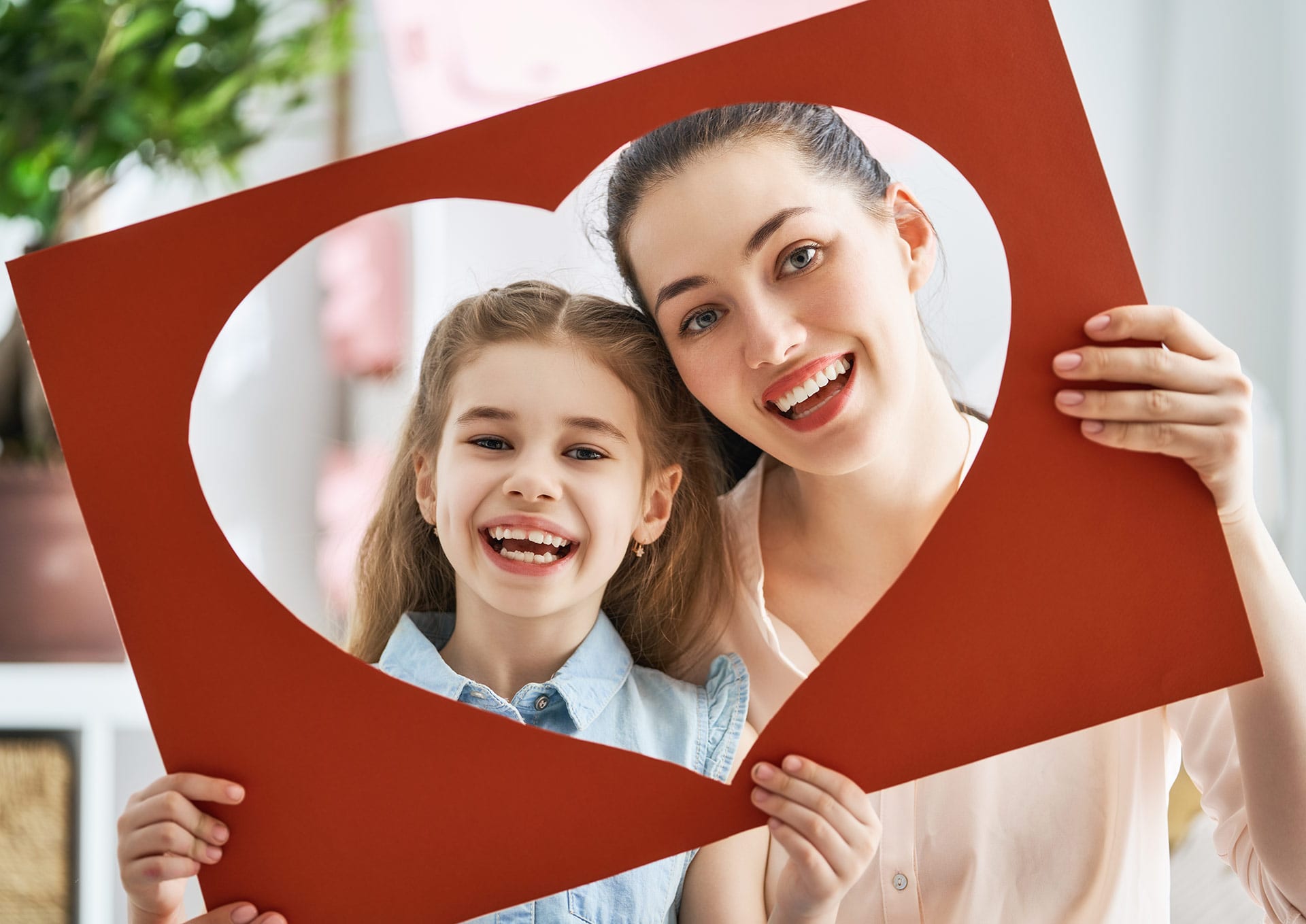 Mother and daughter smiling through a large cutout heart frame after strightening their teeth