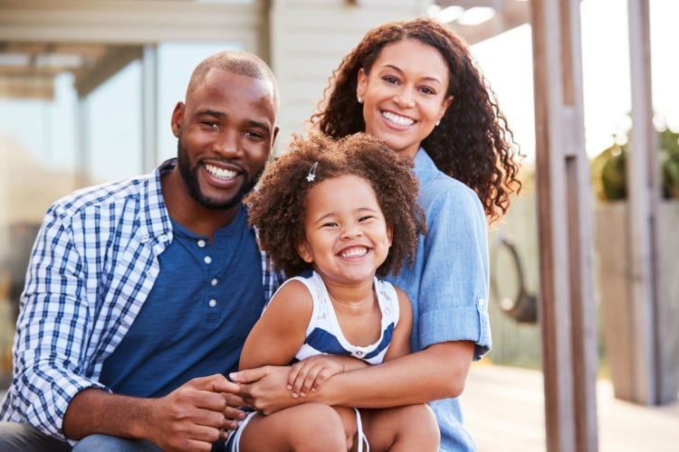 young family embracing outdoors and smiling