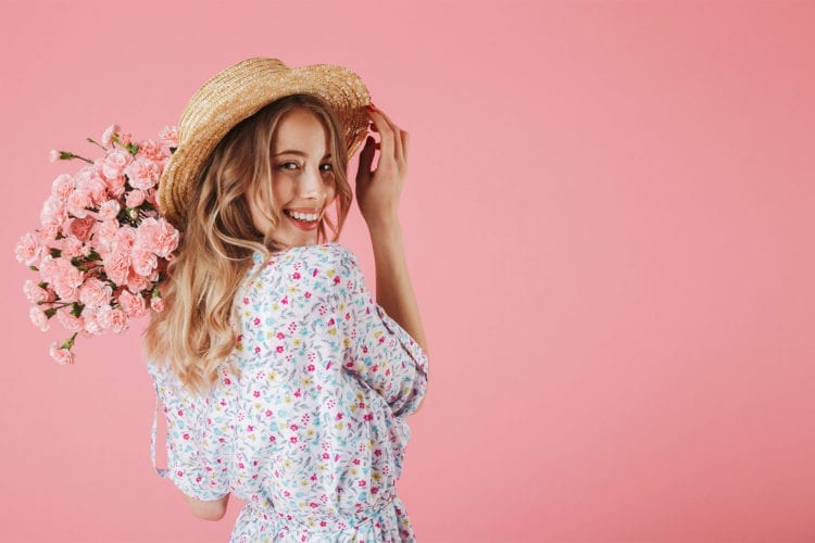 smiling young woman wearing a hat and holding bouquet of flowers