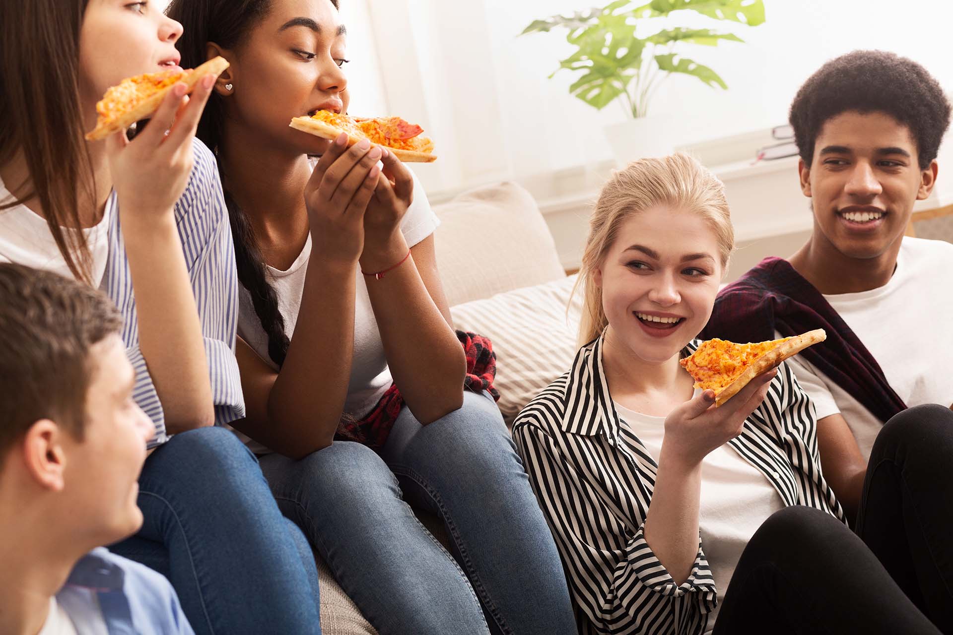 A group of teenage kids visiting and eating pizza after taking out their aligners