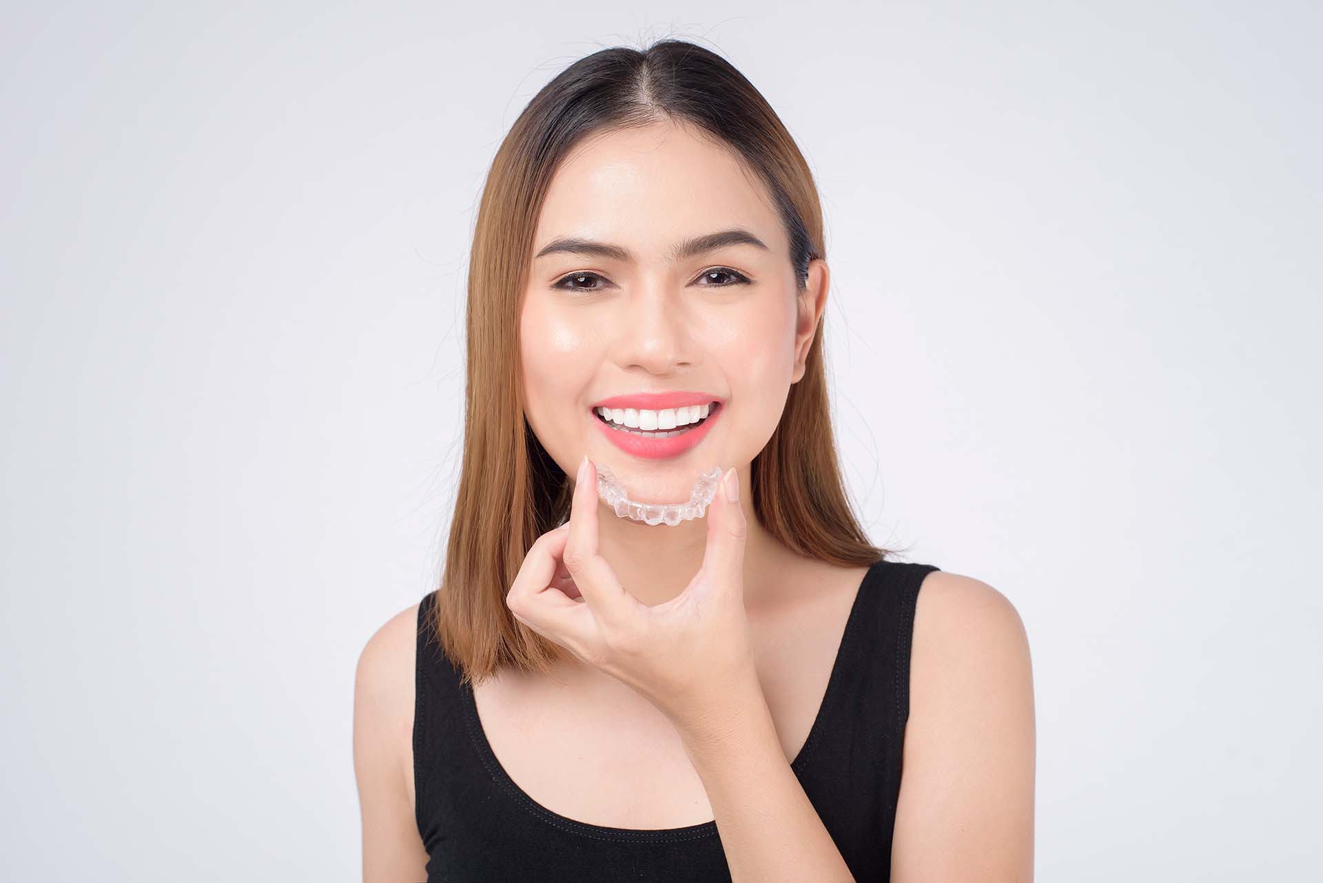Young woman smiles as she inserts a 3M Clarity clear aligner in Geo City