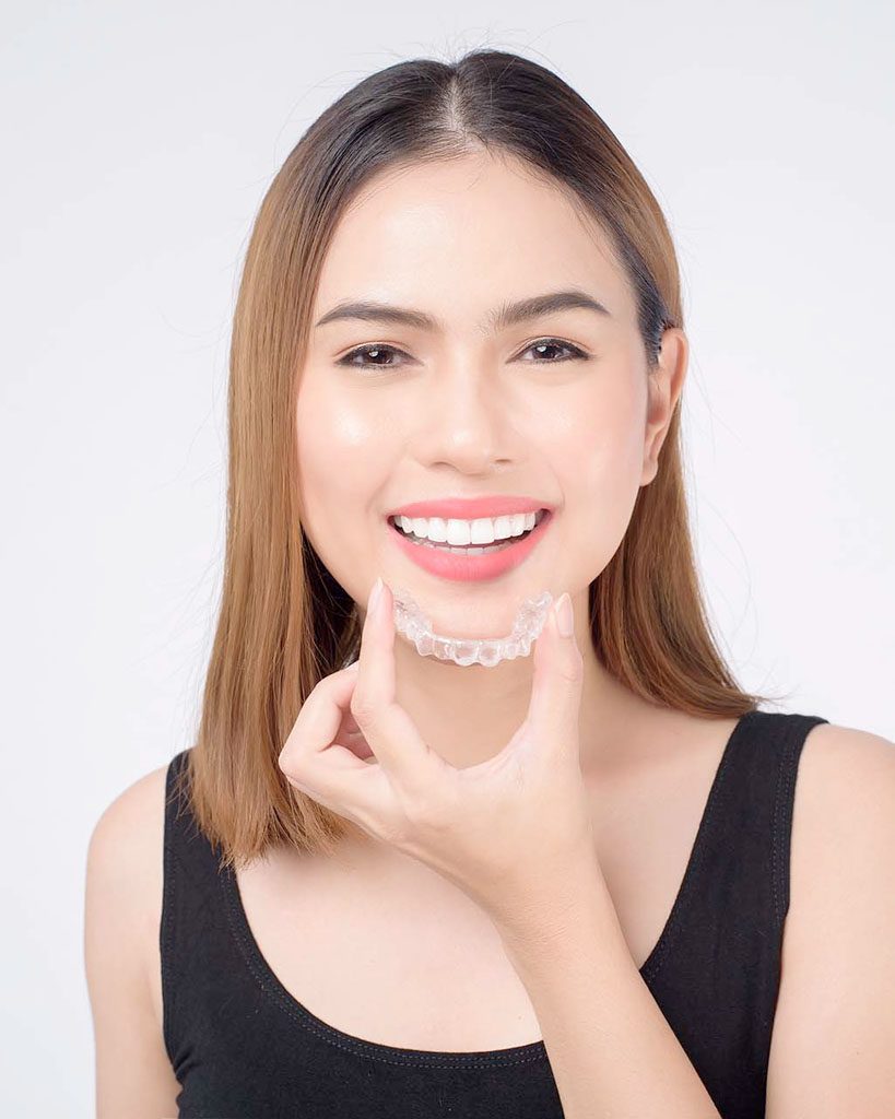 Woman holding a clear aligner in front of her mouth