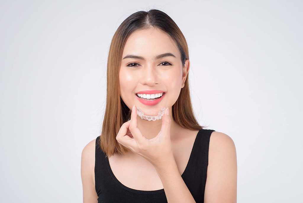 Land Park woman smiles as she inserts clear aligner 