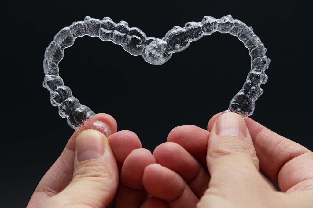 Man holding two Invisalign aligners in a heart shape.  Learn about the average cost of Invisalign treatment and get a free consultation.