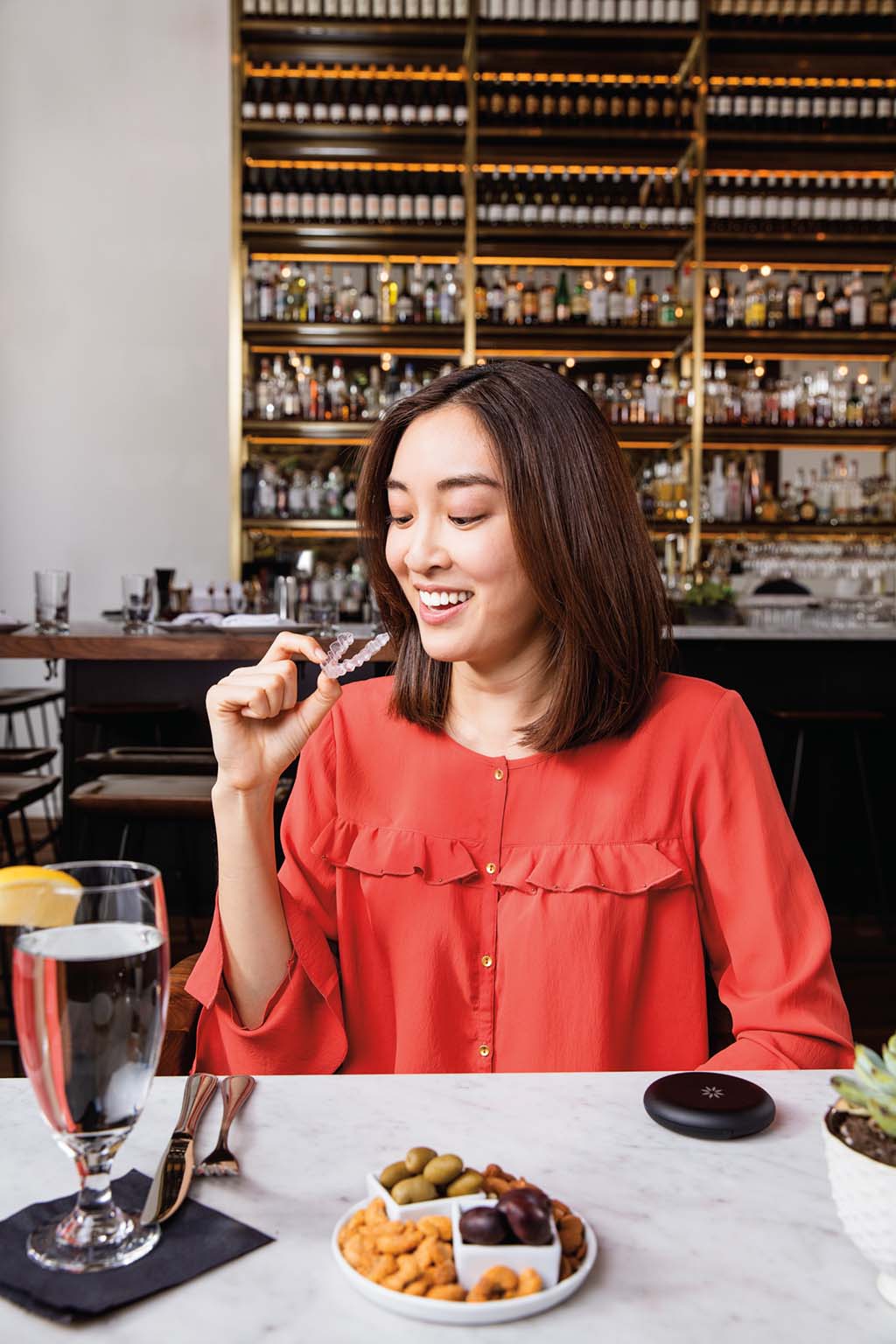 Woman at a restaurant holding her teeth straightening aligner that's fixing her upper teeth