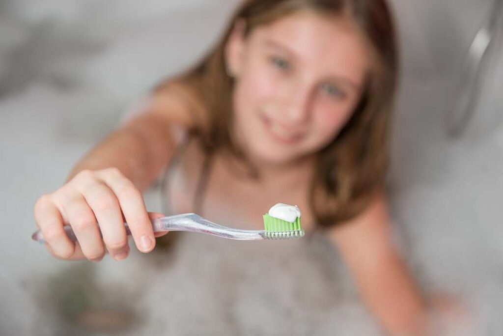 Little girl holding toothbrush with toothpaste in the bathroom