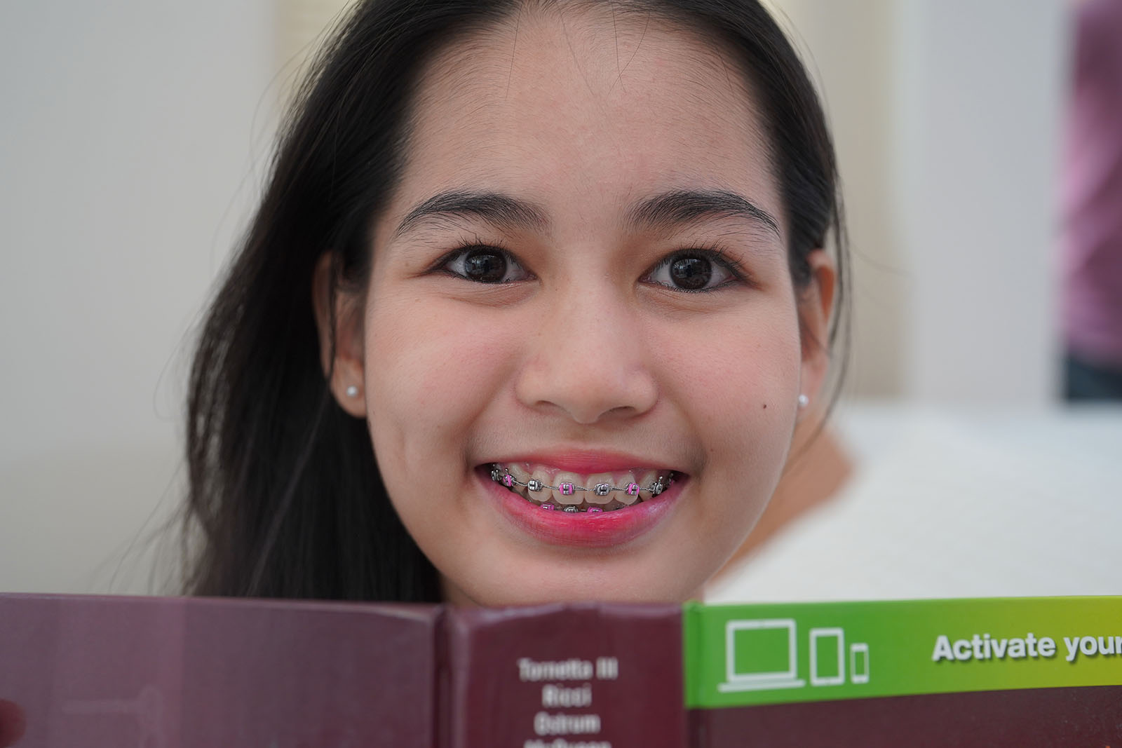 smiling teenage girl with multi-colored braces reading a book