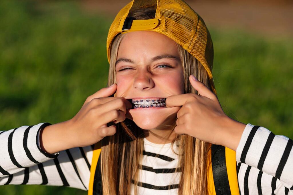girl in backwards cap pulling back her cheeks to show off her braces