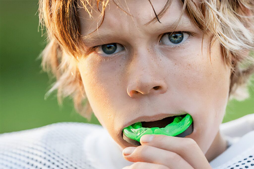 young football player inserts a green mouthguard
