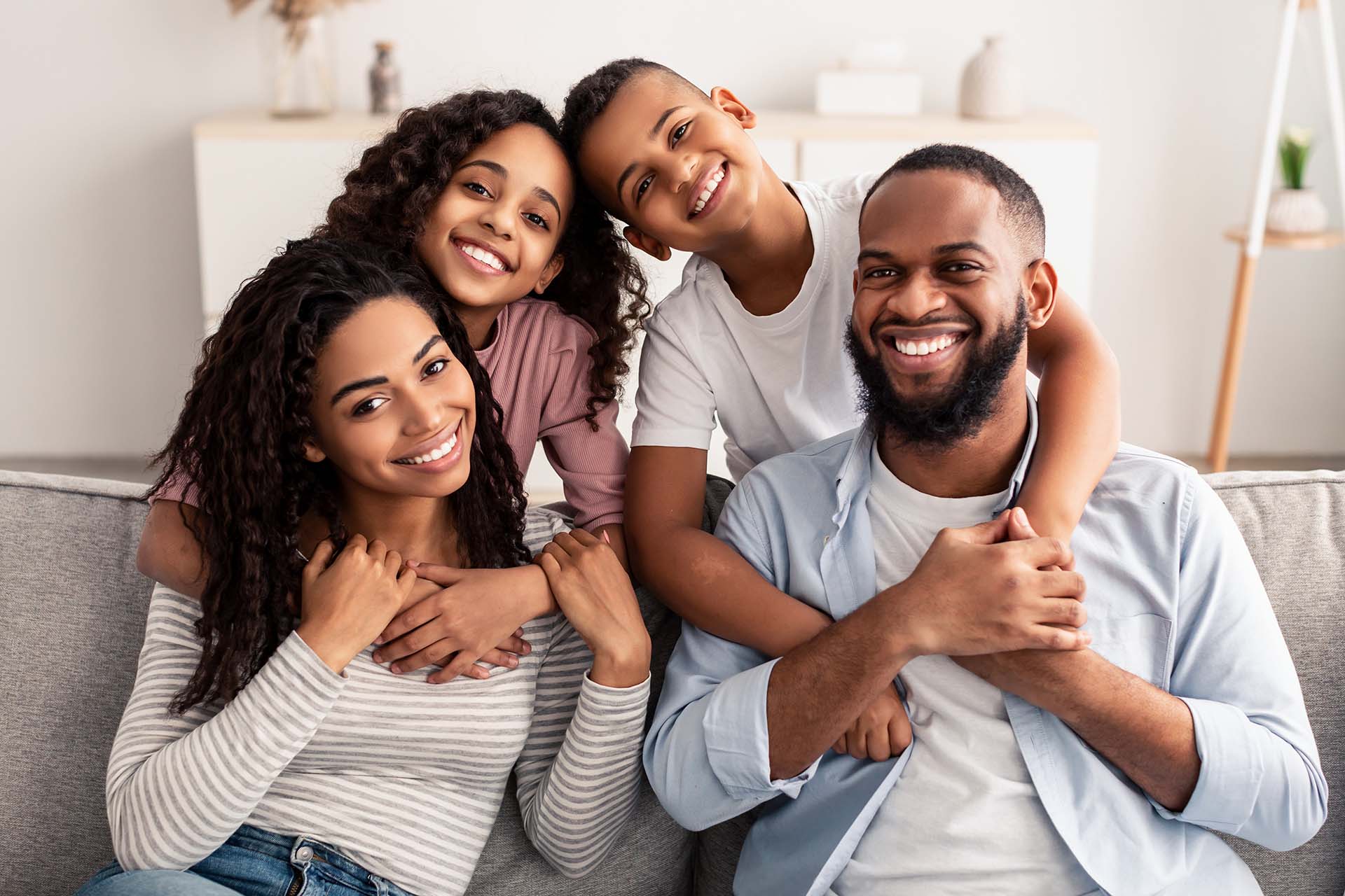 Straight teeth provide health benefits in addition to a pretty smile. Smiling young family relaxing on the couch at home.