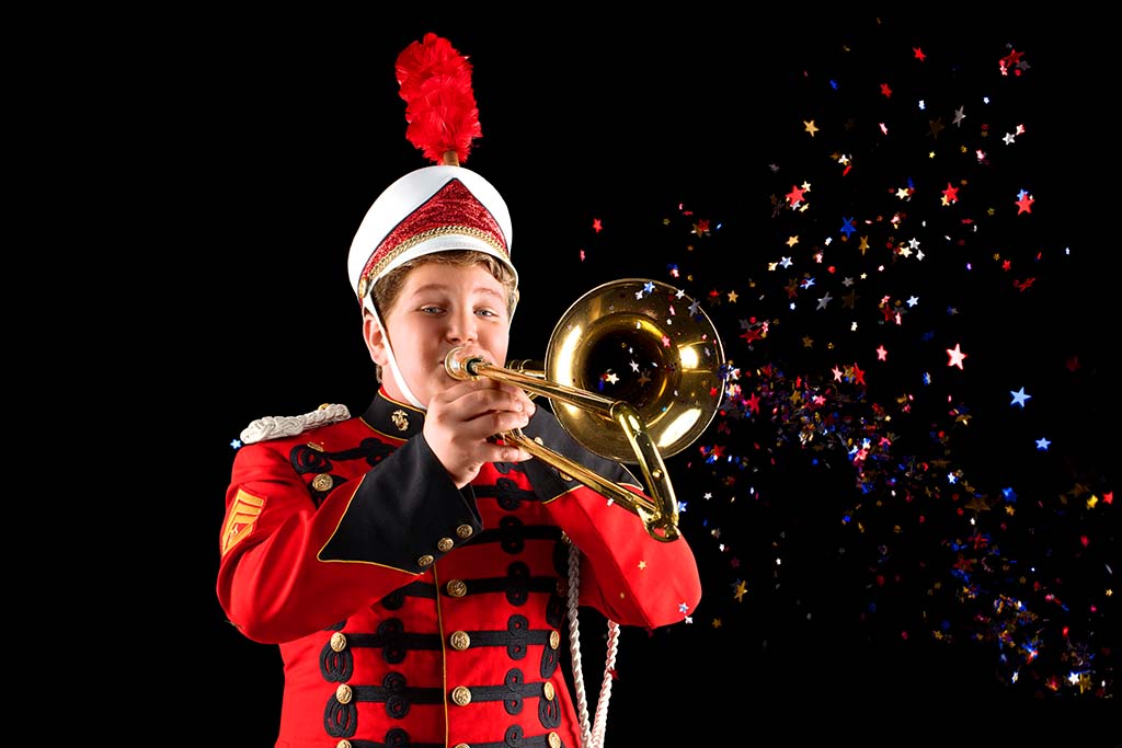 teen boy in marching band playing his trombone in front of a black background