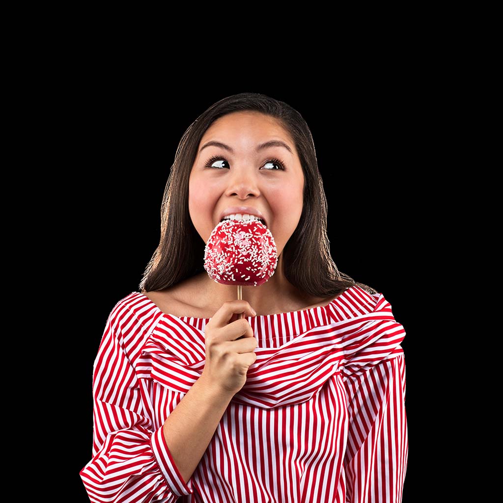 Happy teen girl enjoying a candied apple in front of a black background