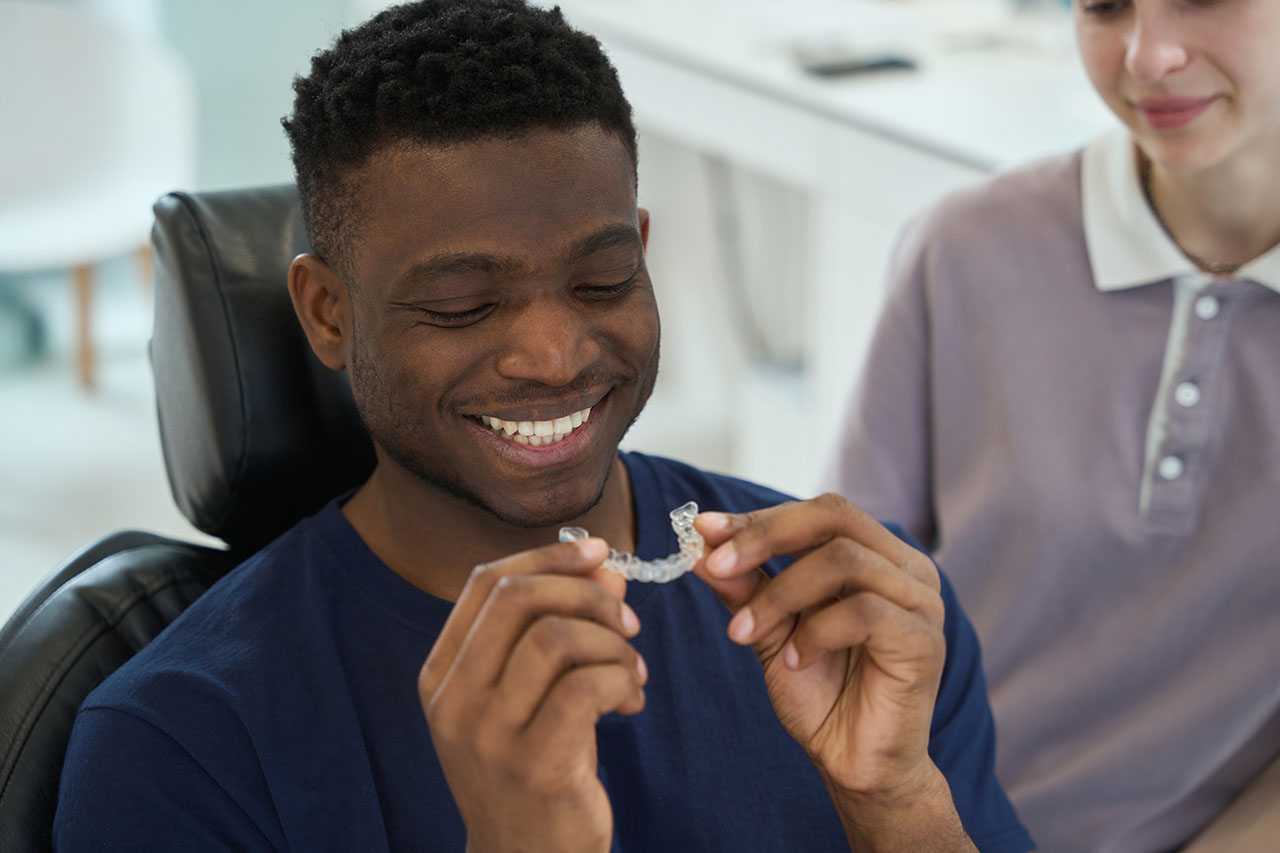 The orthodontist can offer many types of retainers such as Essix retainers A young man at the orthodontist office smiles as he examines his Essix retainer